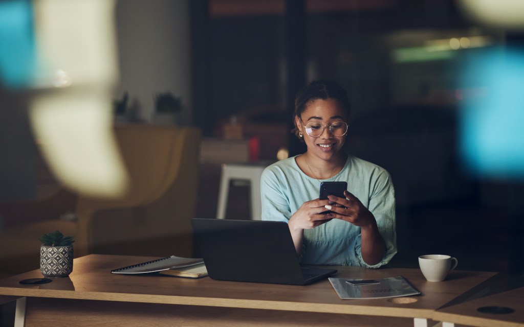 Woman in dark office with phone, typing or reading email, message or social media post connectivity. Late night at work, cellphone and girl at desk networking, online chat or writing text at overtime.